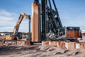 Wabenaushub zum Bodenaustausch: Ansicht eines Bohrgeräts mit mäklergeführtem Rüttler und Bagger mit Langarmgreifer