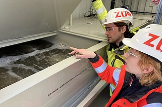 Zu sehen ist ein Foto auf dem zwei Personen eine Pilotanlage des Bioreaktors für eine effiziente Grundwassersanierung begutachten.